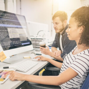 An image of two people working in tandem on a coding project for their tech company.