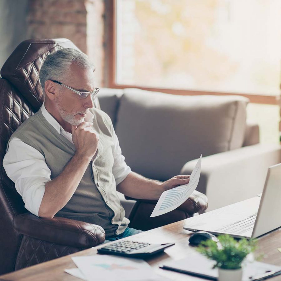 An image of an experienced business investor reviewing a proposal at his office desk.